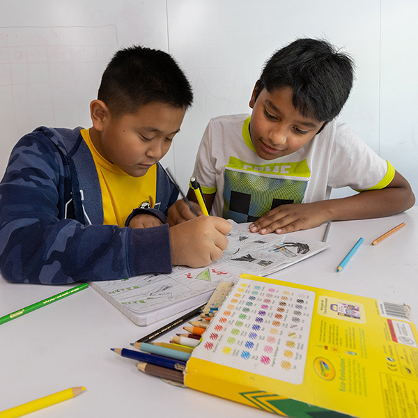 Two Young Writers Institute participants write in a notebook using colored pencils.