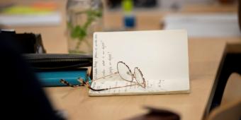 Open notebook on table with glasses keeping the pages open. 