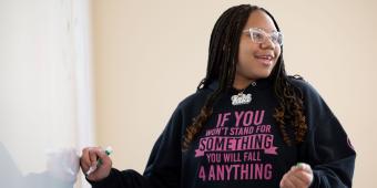 Girl in black and pink hoodie writing on white board 