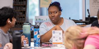 College student sitting at table with two younger students who are writing. 