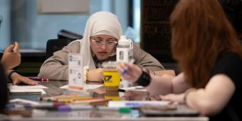 Girl writing poetry at classroom table with fellow students.