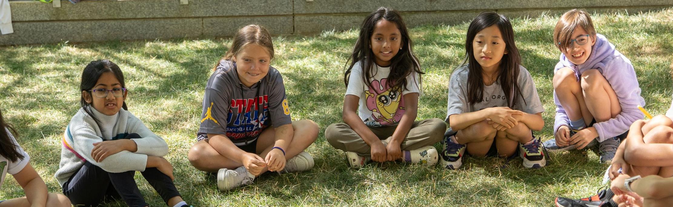 Children sitting in circle outside on the grass.