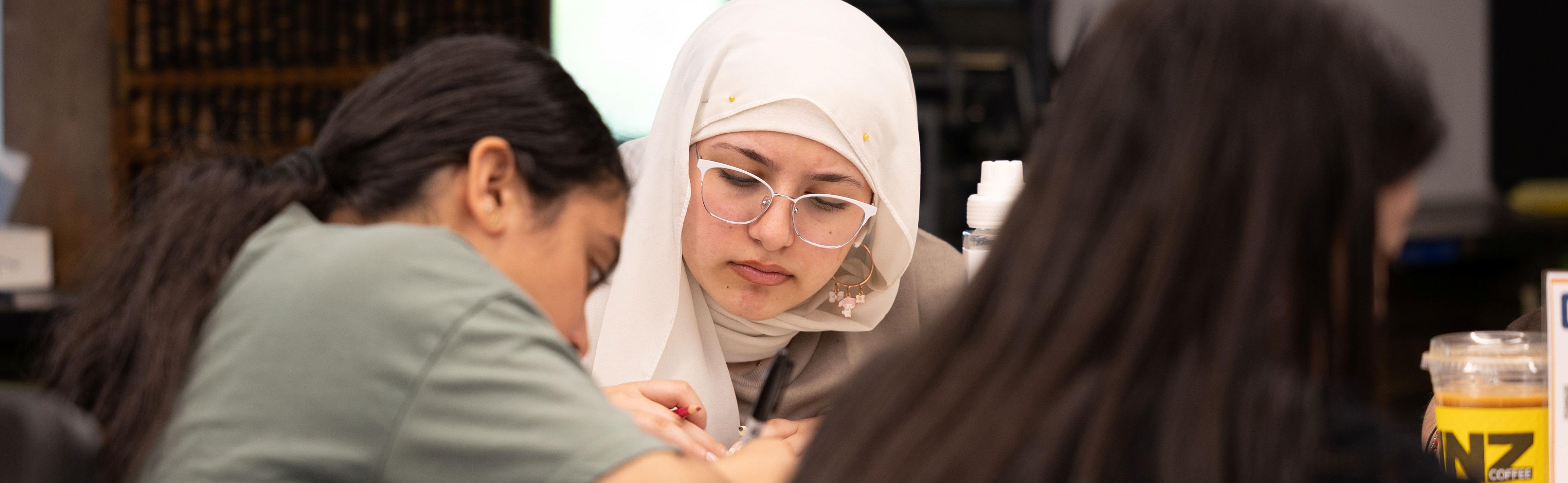 Three high school aged girls write at a table.